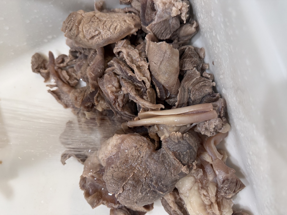 Vigorously hand-washing parboiled beef tendon piece by piece under cold running tap water